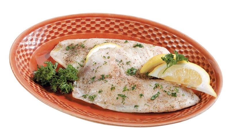 Tilapia with garnish and lemon wedges in dark colored dish Food Picture